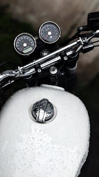 Detailed close-up of a motorcycle handlebar and speedometer, covered in raindrops, emphasizing texture and detail.