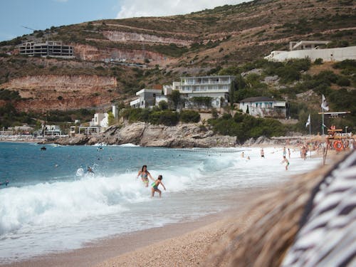 Free People Relaxing on a Summer Beach with Hillside Houses in the Background Stock Photo