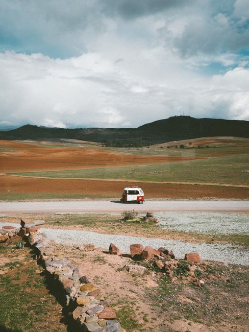 A scenic drive in Cusco's rural landscapes with a classic van on a dirt road.