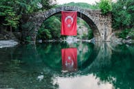 一座石桥的宁静景色中，土耳其国旗倒映在下方的水面上