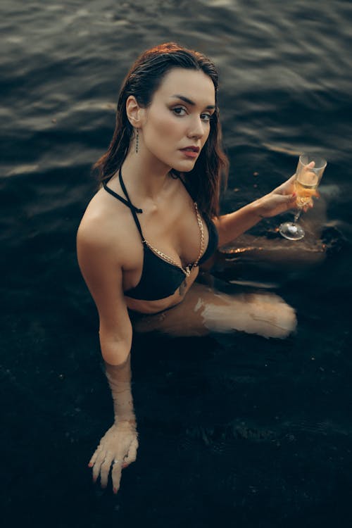 A woman in a bikini sitting in the water holding a glass