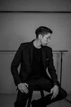 Elegant black and white portrait of a man in glasses posing in a studio setting.