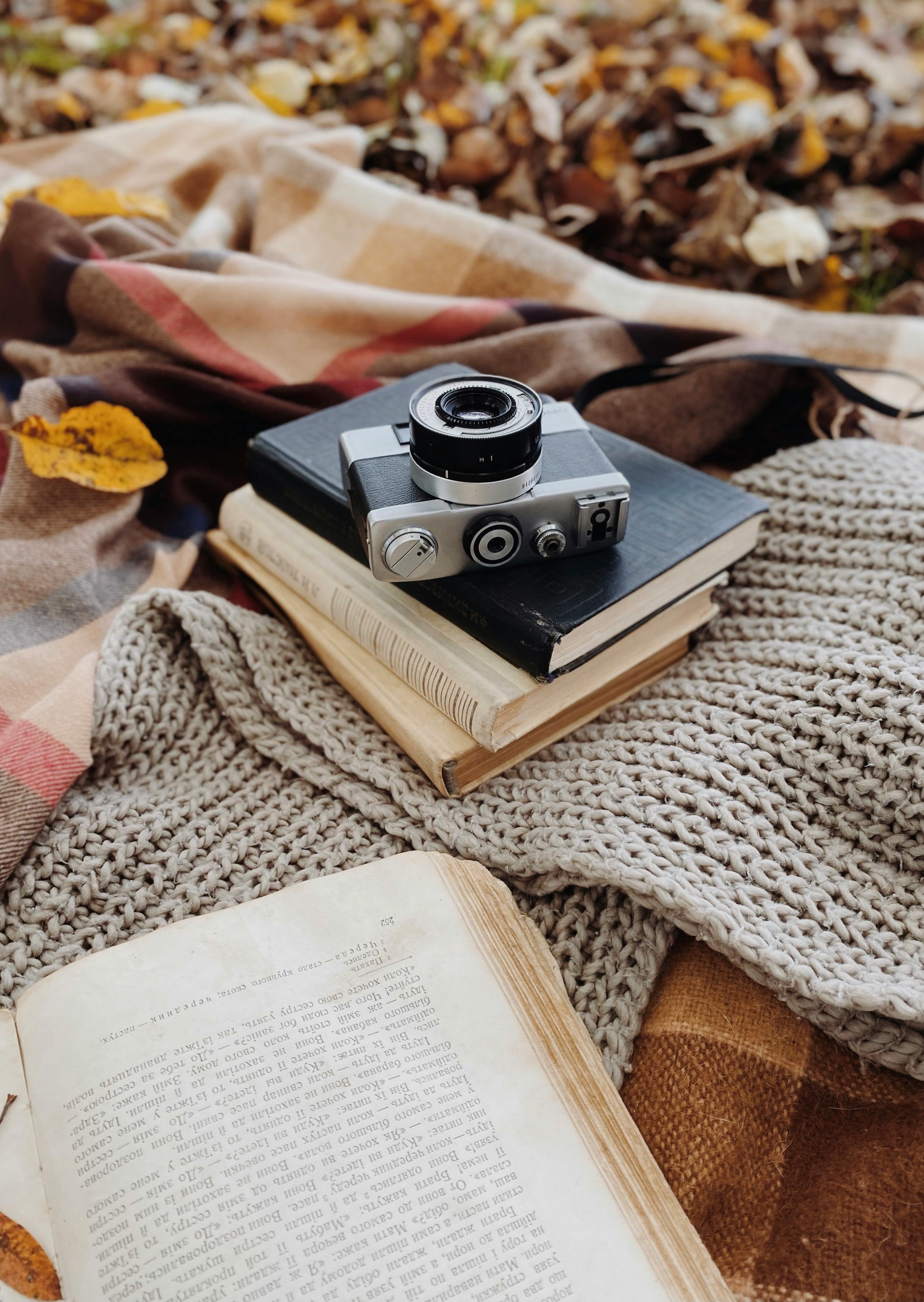 A vintage camera on books amidst a knitted scarf, capturing an autumn theme.