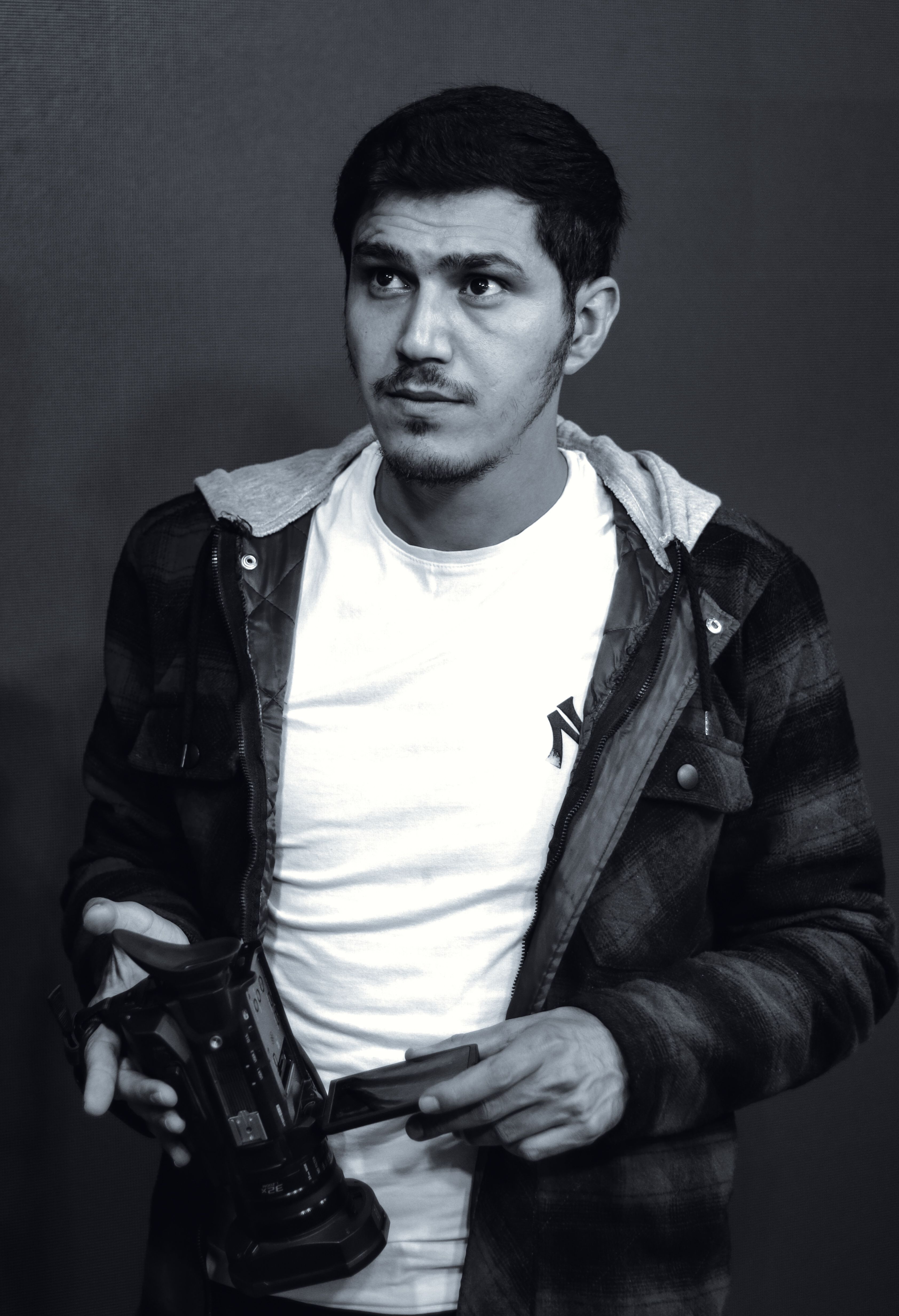 Young man holding a camera, dressed casually in a t-shirt and jacket.