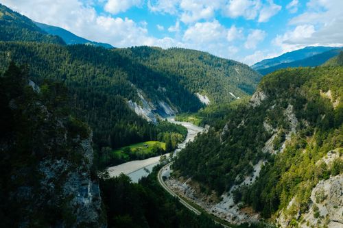Free A captivating view of a lush green alpine valley with a meandering river and a road cutting through the landscape. Stock Photo