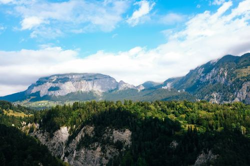 Free A stunning view of mountainous landscapes with lush green forests under a bright blue sky. Stock Photo