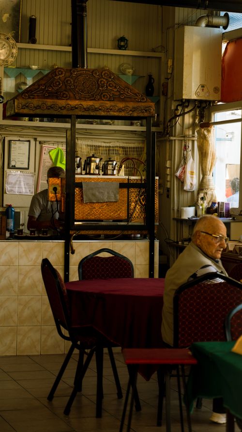 Free A warm and inviting restaurant interior featuring an elderly man seated near a rustic oven. Stock Photo