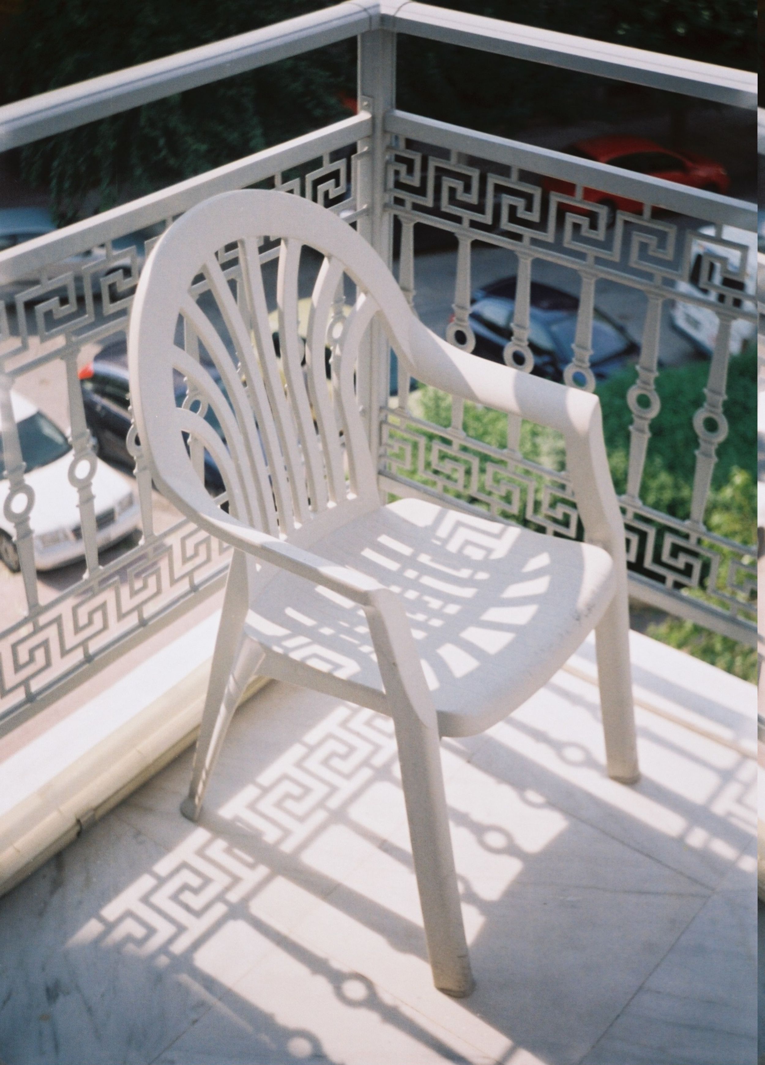 A white plastic chair casting shadows on a sunny Athens balcony.