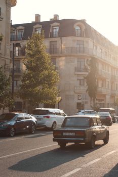 A classic vintage car driving along a sunny urban street by old European architecture.