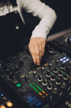 Close-up of a DJ's hand adjusting knobs on a professional sound mixer during a performance indoors.