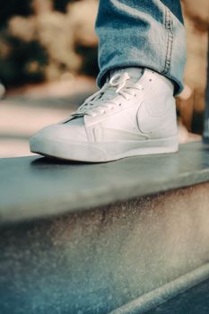 Detailed close-up of a white sneaker on an urban ledge, emphasizing modern footwear style.