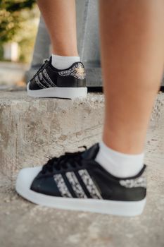 Adidas Superstar sneakers in black with white accents worn on outdoor concrete steps.