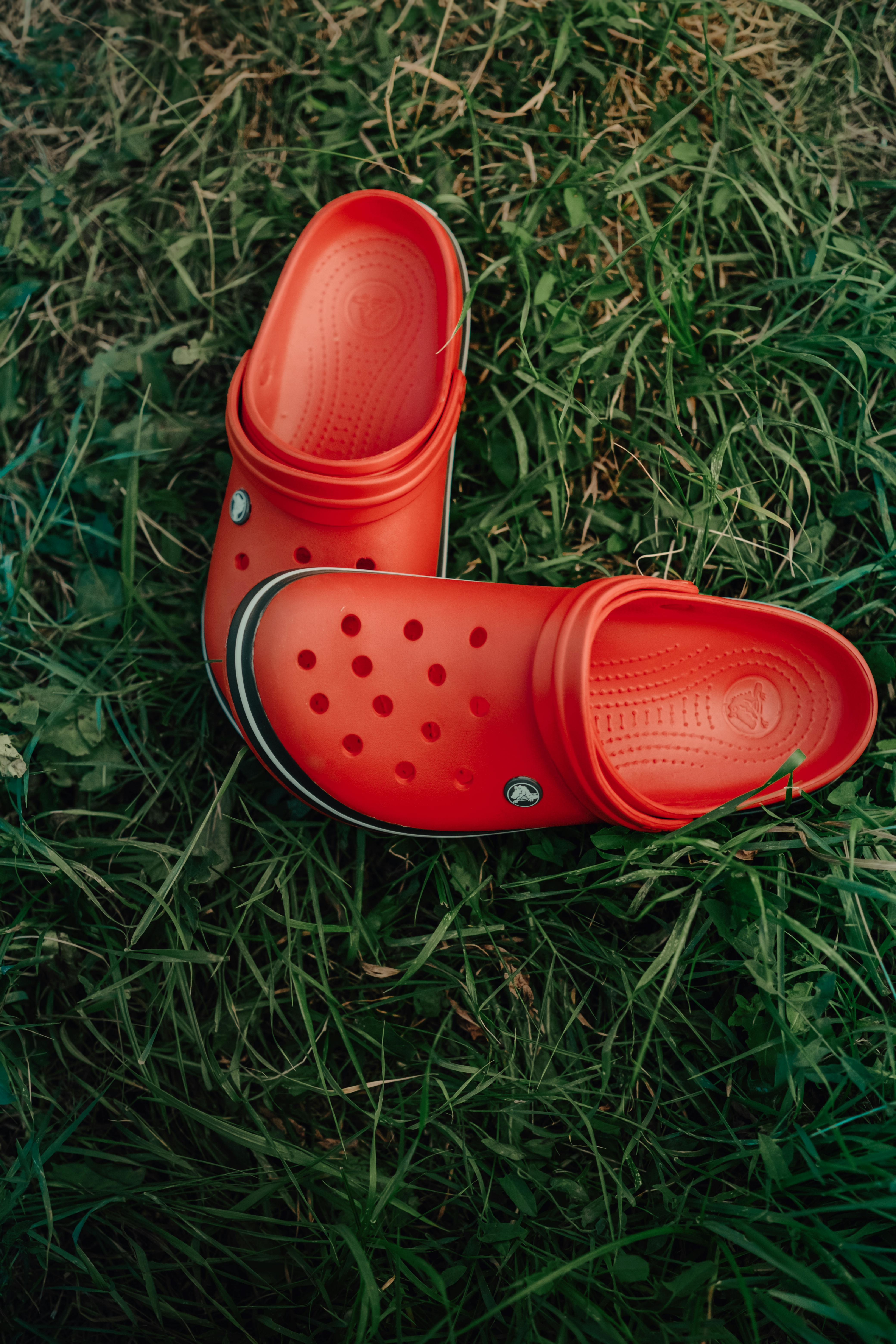 Bright red rubber clogs placed on fresh green grass, showcasing casual outdoor footwear.