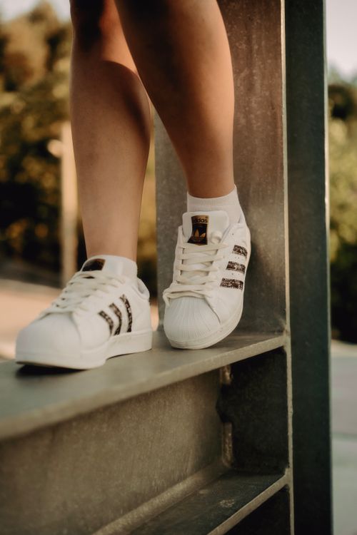 Free Close-up of white sneakers standing on a metal beam outdoors with a blurred background. Stock Photo