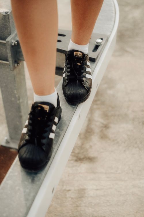Free Black and white sneakers balancing on a metal beam outdoors, showcasing modern footwear fashion. Stock Photo