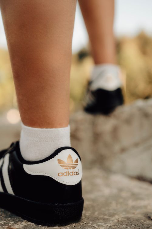 Free Close-up of legs wearing Adidas sneakers outdoors on a sunny day. Stock Photo