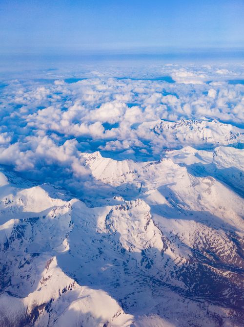 Free Majestic aerial landscape of snow-covered mountain peaks under a sea of clouds, showcasing winter's serene beauty. Stock Photo