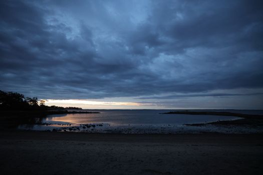 Serene beach at dusk with dramatic clouds and calm waters in Stamford, Connecticut.