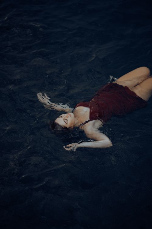 Free Woman in red dress floating peacefully in dark blue water, captured in Fethiye, Türkiye. Stock Photo