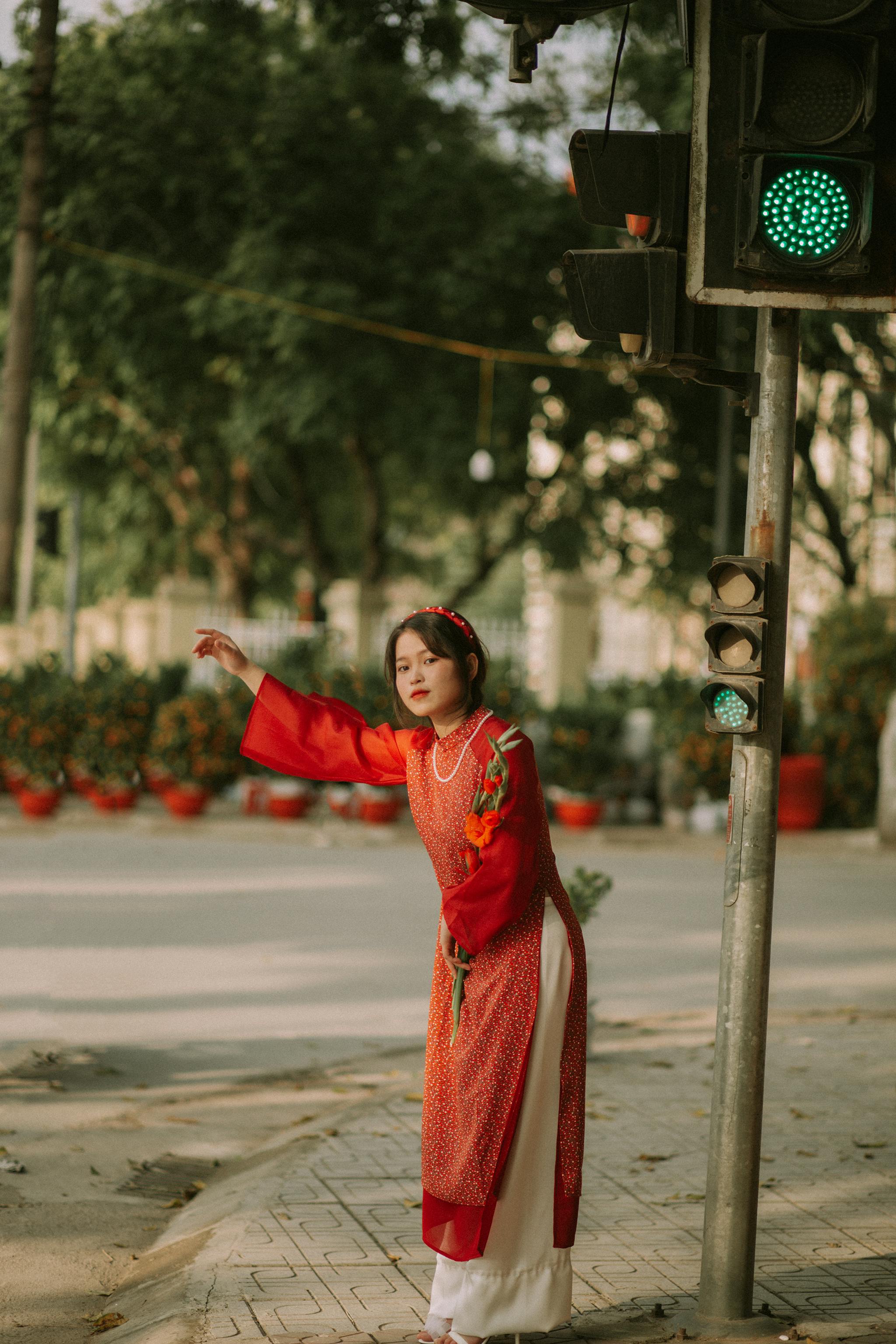 Woman in traditional red Ao Dai near traffic light on a city street.