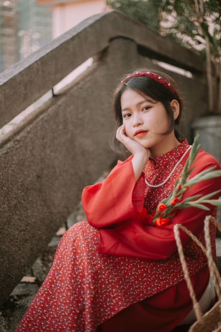 Elegant portrait of a young woman in a red dress holding flowers, seated on concrete stairs.