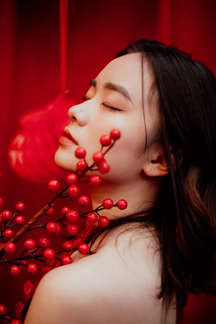 A serene profile portrait of a young woman posing with vibrant red berries against a rich red background.