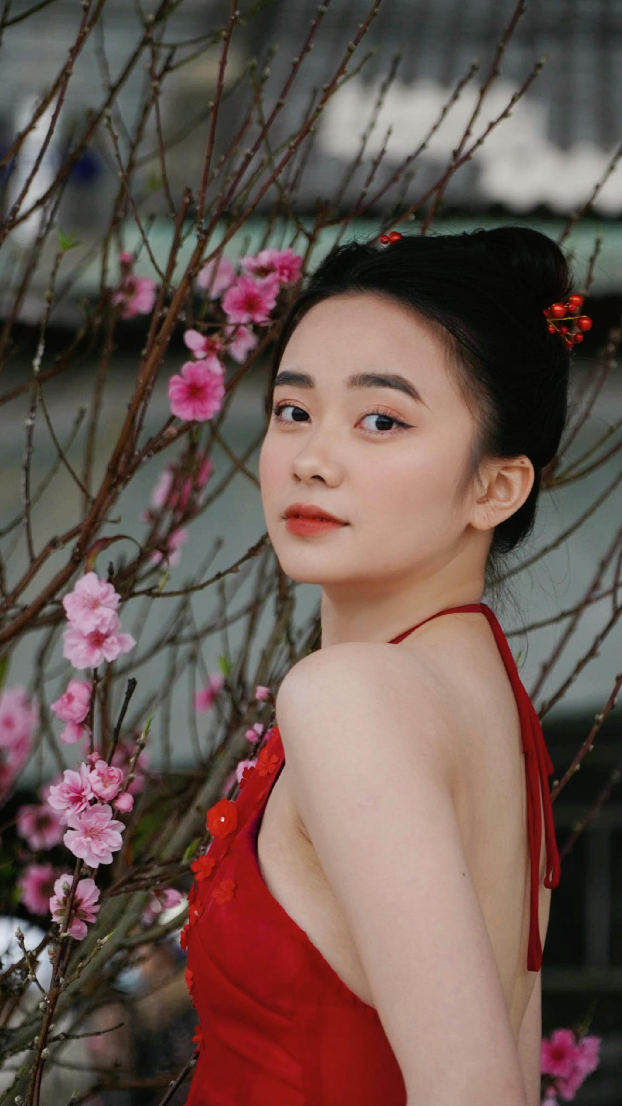 Stylish portrait of a woman in a red dress among cherry blossoms.