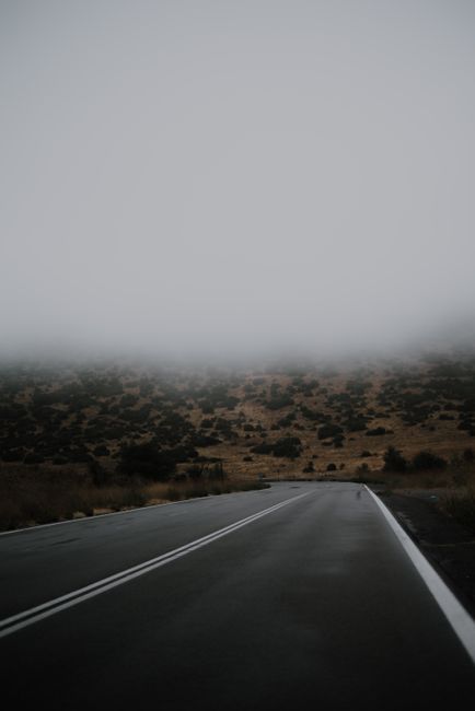 A desolate road vanishes into fog on a mist-covered hillside, creating an ethereal landscape scene.