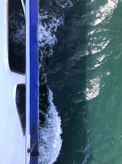 Free Elevated view of ocean waves against a ship, showing dynamic sea foam and vibrant sunlight reflections. Stock Photo