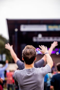 Man raising hands at outdoor concert with audience and bokeh lights.