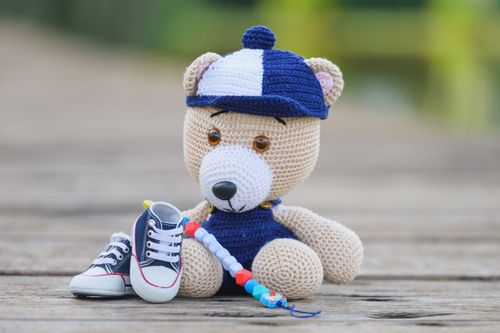 Free Cute crocheted teddy bear with baby shoes and beaded toy on a wooden background. Stock Photo