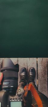 Top-down view of camera and boots on wooden pier by the water.