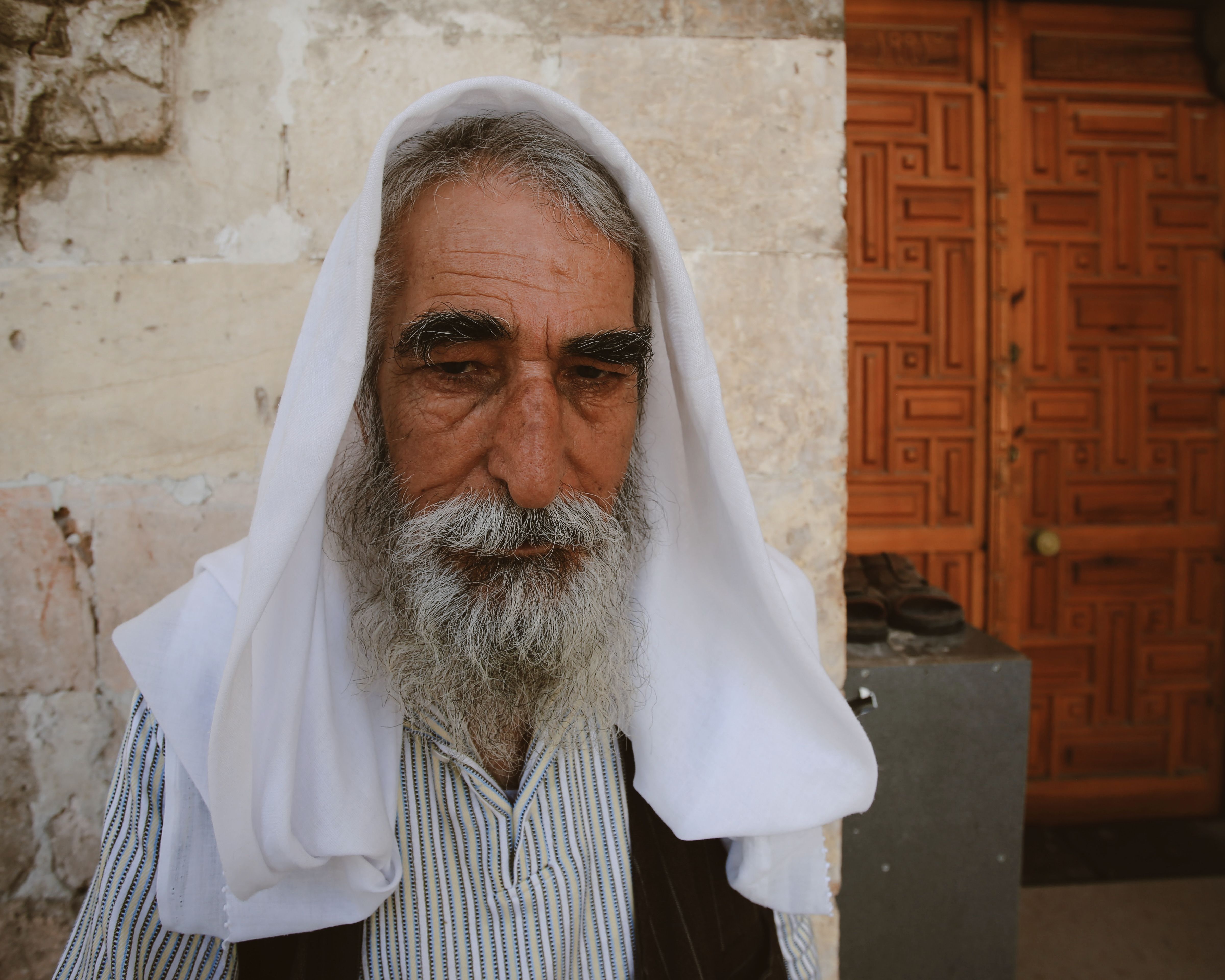 Portrait of an elderly man with a white headscarf in front of ornate wooden door