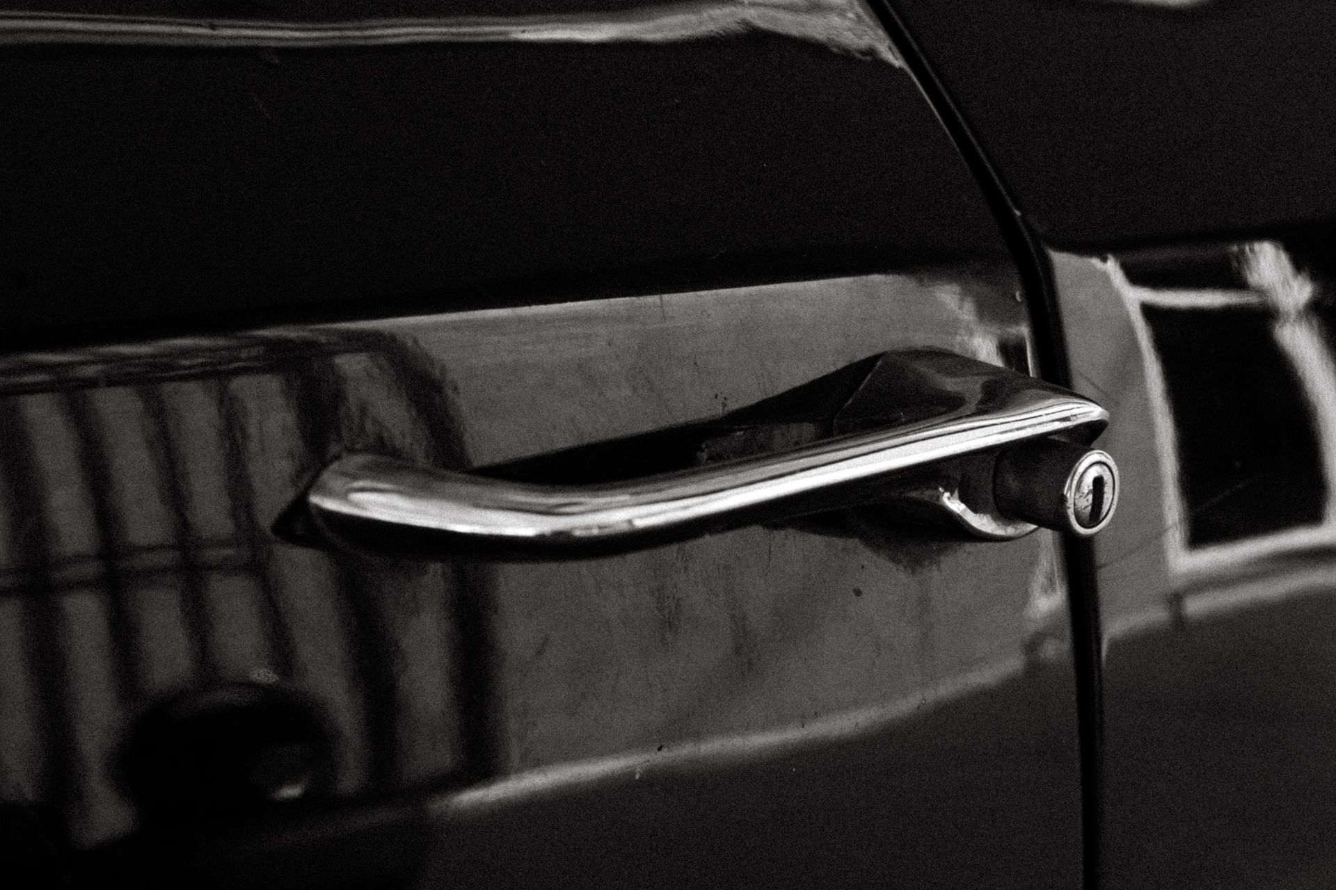 Close-up of a vintage car door handle in a black and white photograph, showcasing retro design.