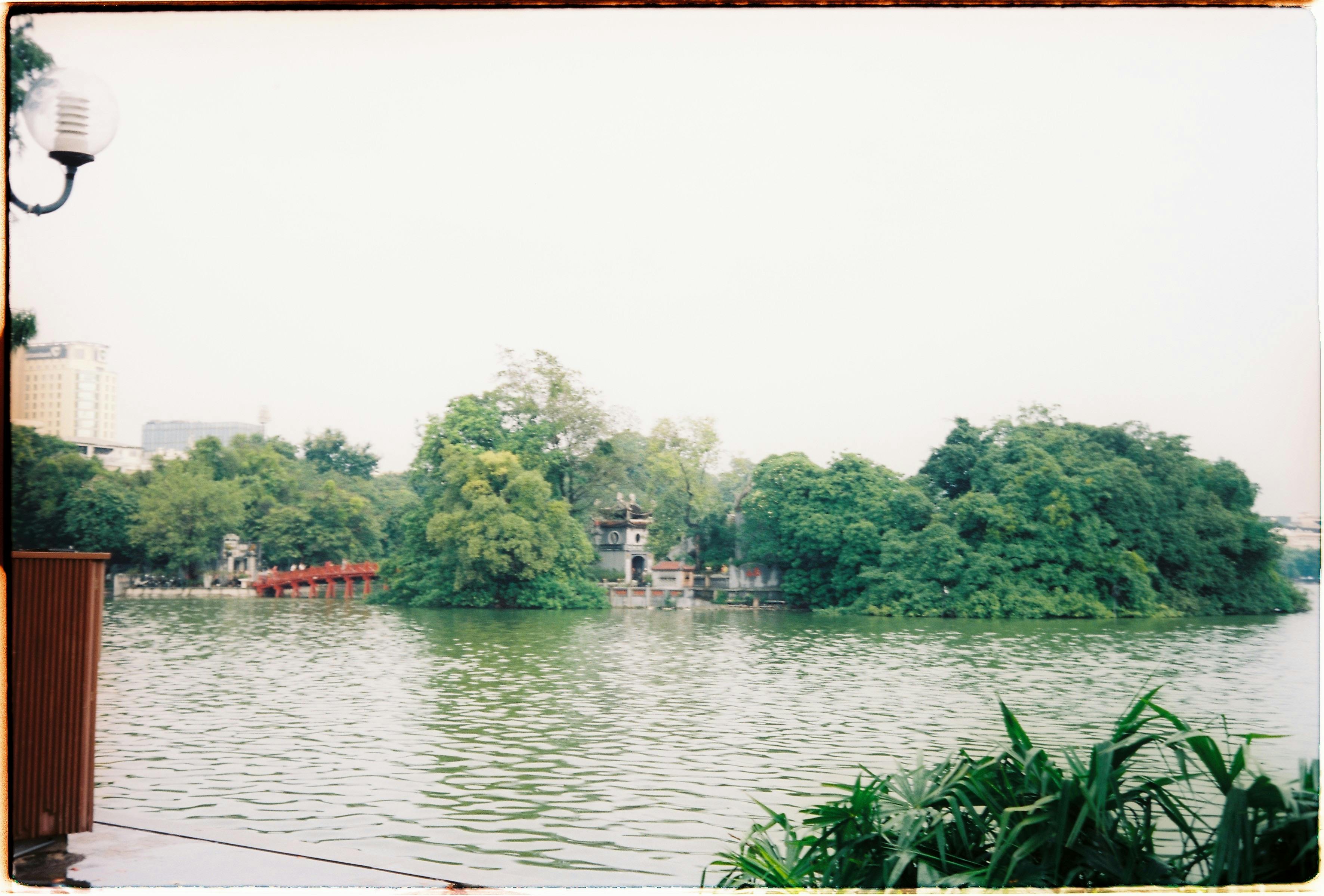 Serene view of Hoan Kiem Lake in Hanoi, featuring Ngoc Son Temple and lush greenery.