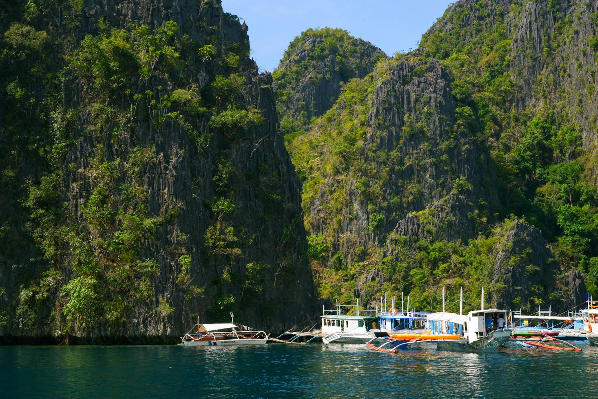 Traditional boats moored by rugged limestone cliffs in Coron, Philippines offer a stunning tropical escape.