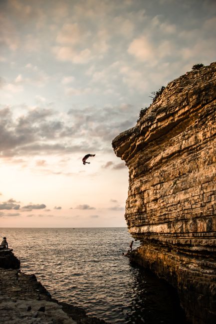Silhouette of a diver leaping off a cliff into the ocean at sunset, capturing adventure and freedom.