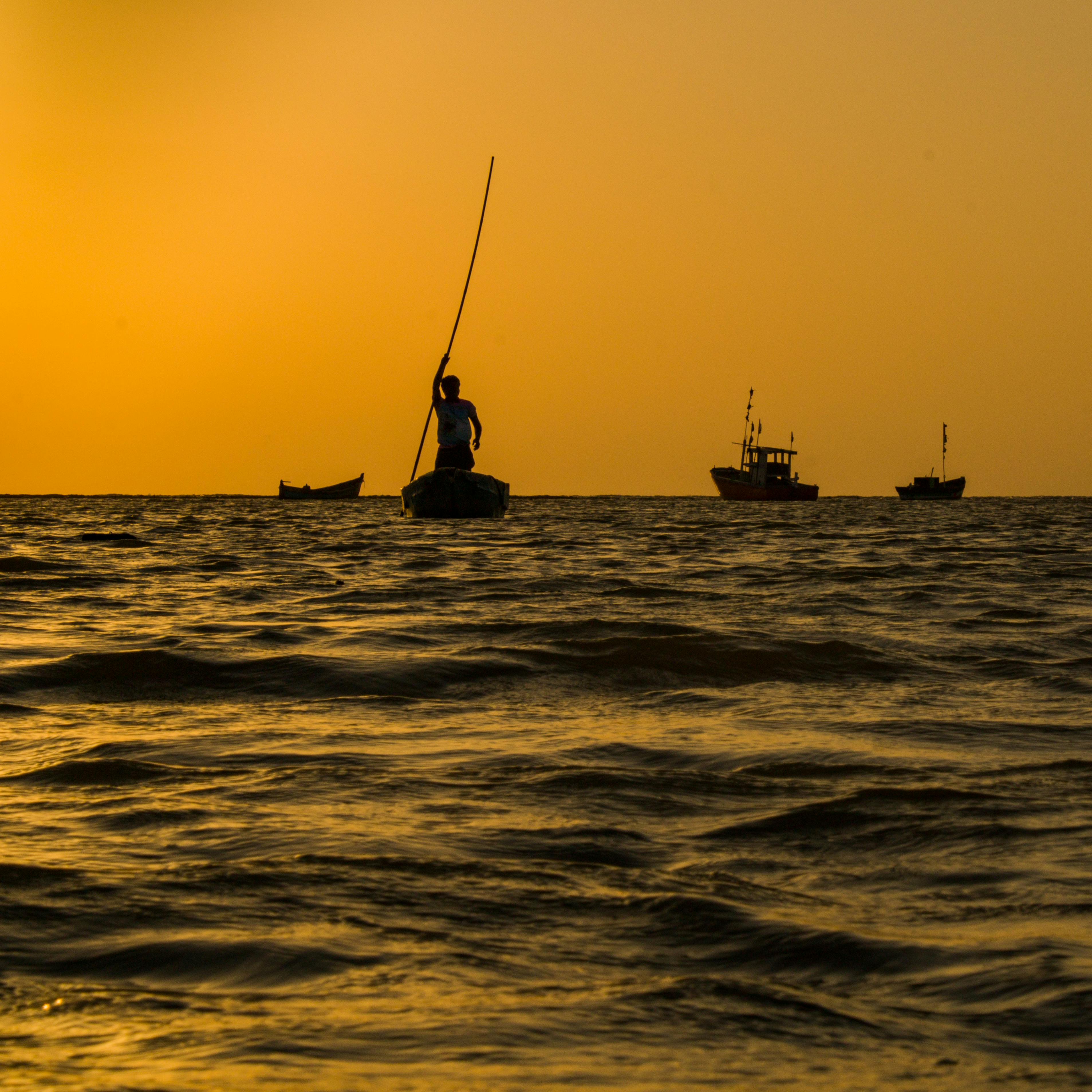 Silhouette of a fisherman rowing at sunrise in the waters of Maharashtra, India.