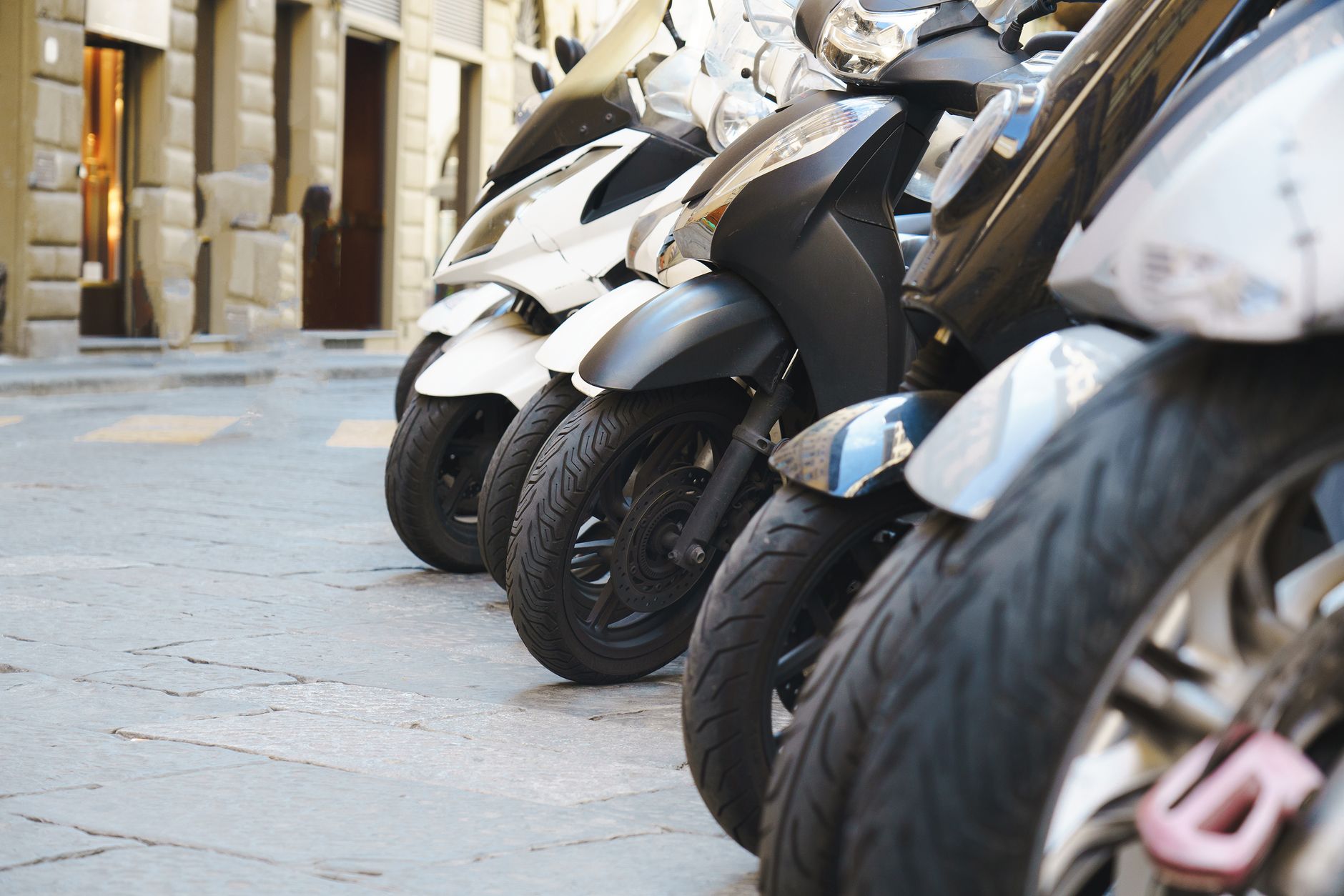 Close-up view of parked scooters lined up on a city street, showcasing urban transport trends.