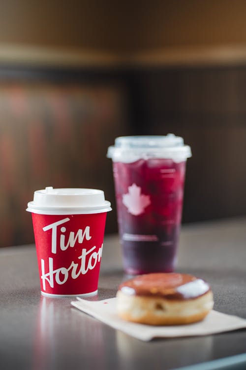 Disposable Coffee Cup from Tim Hortons Chain Restaurant Next to a Donut and a Cup of Cold Drink