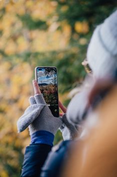 A woman captures vibrant autumn foliage in a Quebec forest using her smartphone.