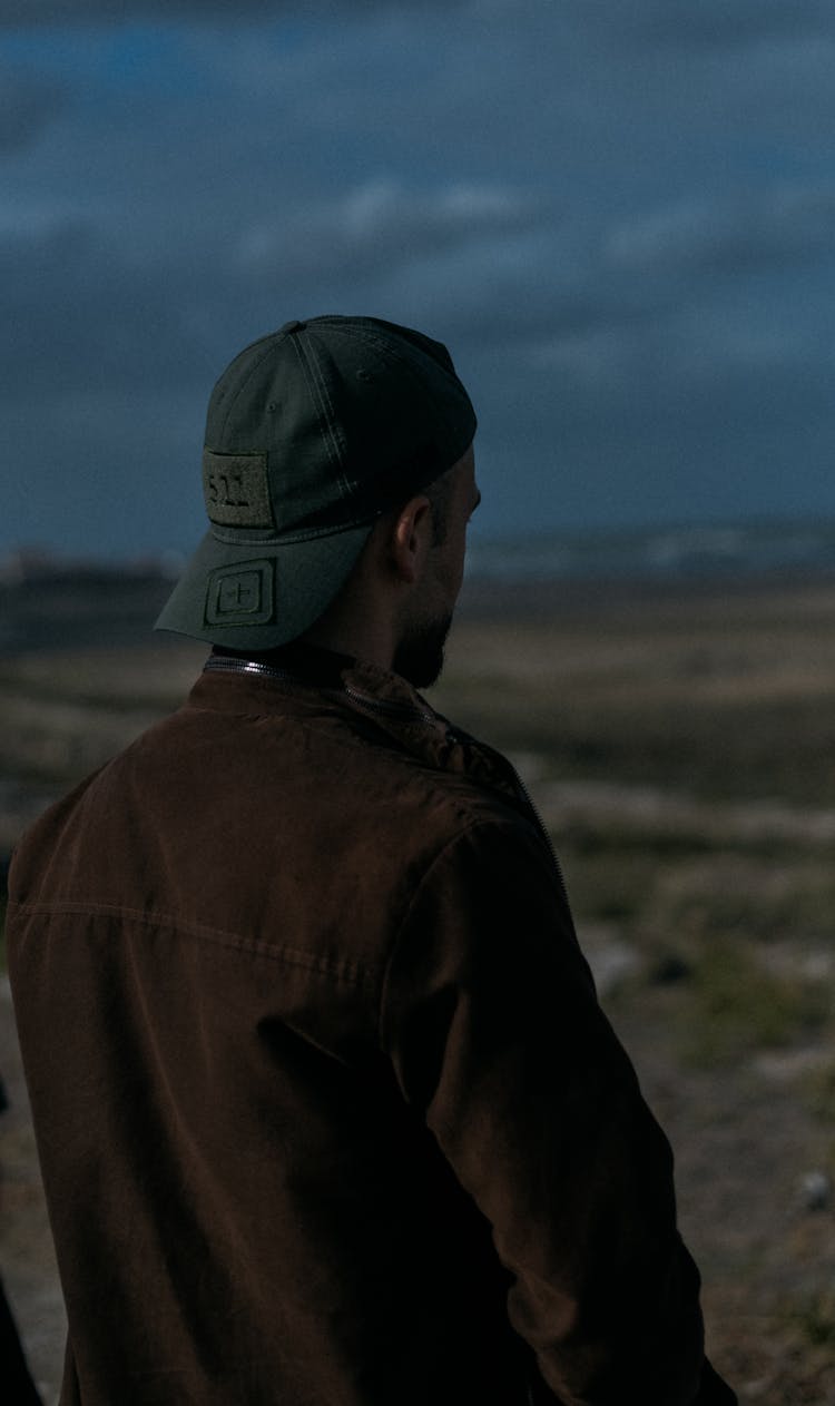 Back View Of A Man In A Brown Jacket And A Cap Standing Outside