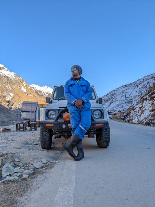 Free A man in a blue suit poses confidently by an SUV on a snowy mountain road in Manali. Stock Photo