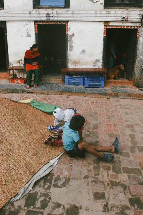 Children Sitting on Pavement in Town