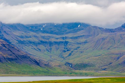 Breathtaking view of Iceland's rugged mountains with cloud coverage and lush greenery.