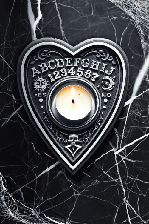 Free A candle flickers on a gothic Ouija board planchette, setting a mysterious Halloween mood. Stock Photo