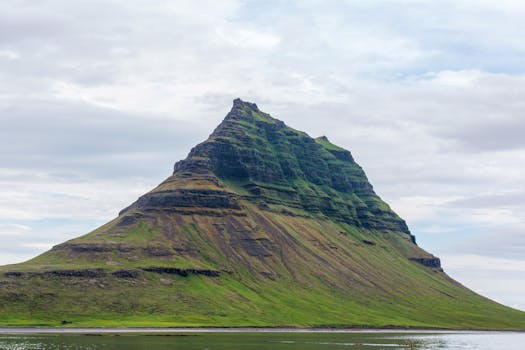 Majestic view of Kirkjufell Mountain with lush greenery under a cloudy sky.