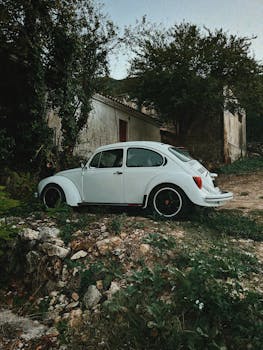 A classic white Volkswagen Beetle parked by an old rustic building in a Lefkada village.