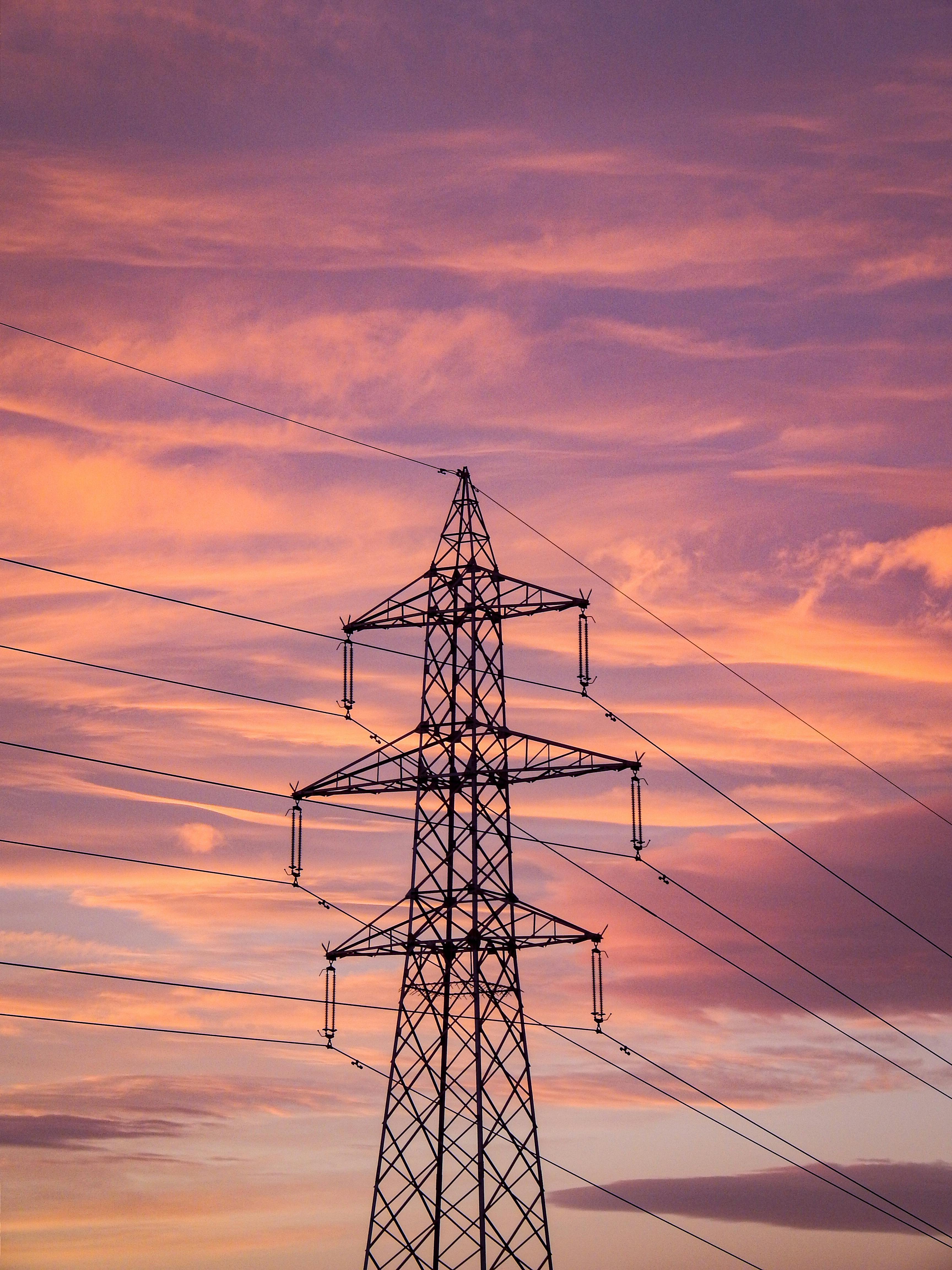 Silhouette of a power transmission tower set against a vibrant pink and orange sunset sky.