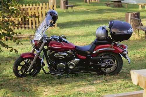 Free A sleek red motorcycle parked on grass in a sunny park, featuring a shiny helmet and scenic surroundings. Stock Photo